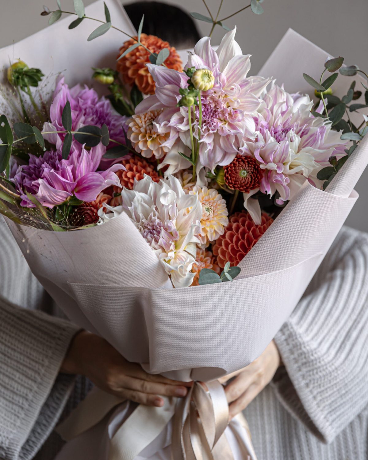 A woman holds in her hands a large festive bouquet with chrysanthemums and other flowers.